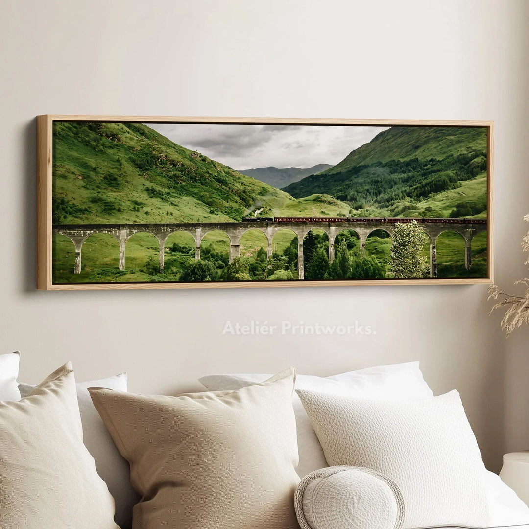 Long horizontal Glenfinnan Viaduct wall art featuring the Jacobite steam train crossing the iconic Scottish railway bridge, framed in natural wood and styled above a neutral sofa in a modern living room.