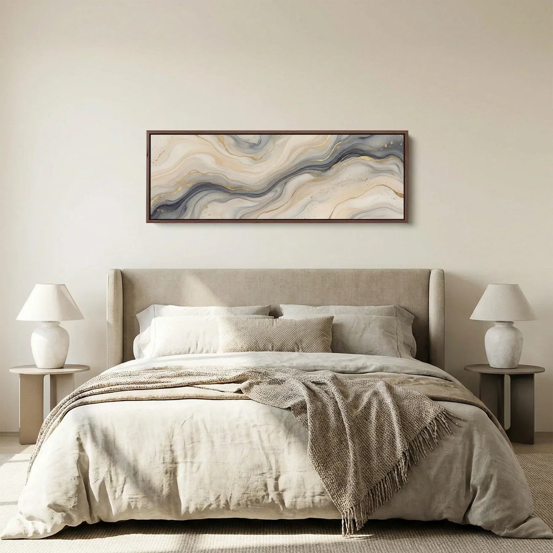 Framed narrow horizontal abstract wall art in neutral beige, grey and cream tones, styled above a bed in a modern minimalist bedroom.